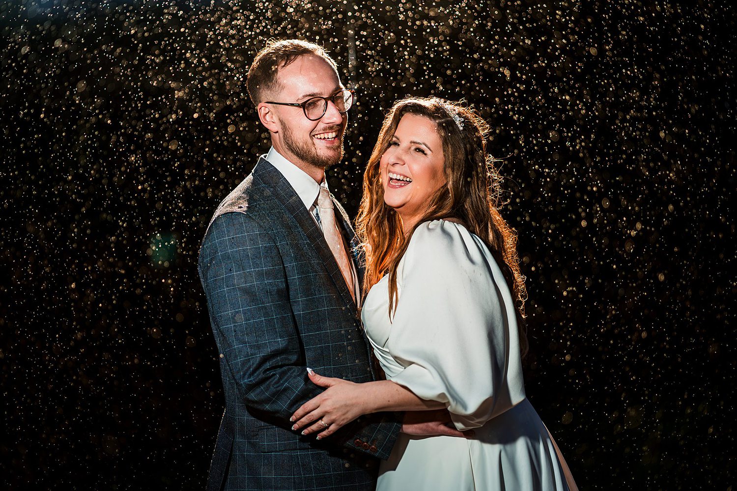 Smiling couple embraces under evening rain.