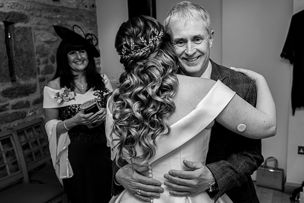 Bride hugging man at wedding, woman in background smiling.
