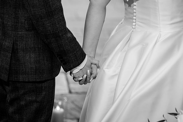 Bride and groom holding hands, wedding attire, black and white.