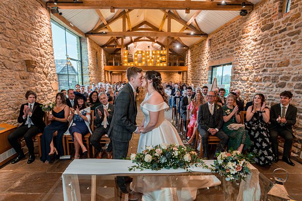 Bride and groom kissing at rustic wedding ceremony.