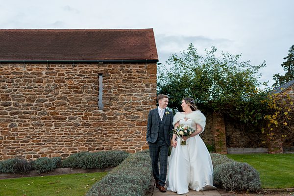 Couple in wedding attire by stone building.