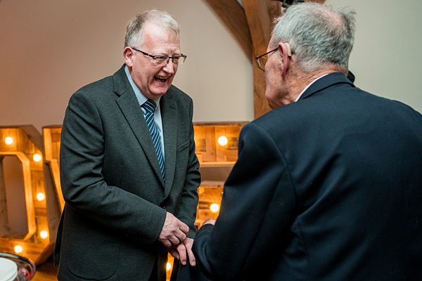 Two men shaking hands and conversing at an event.