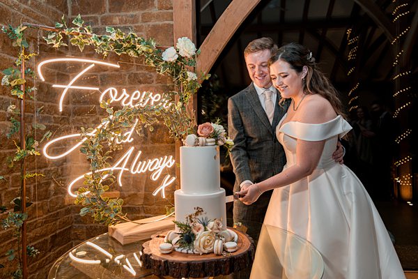 Couple cutting wedding cake under "Forever and Always" sign