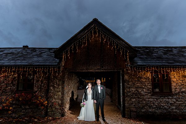 Couple outside stone building with fairy lights at dusk.