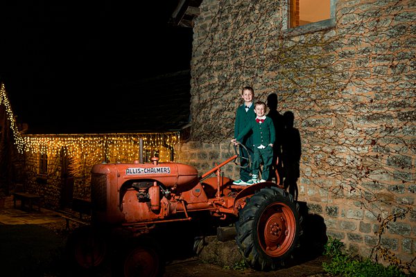 People with vintage tractor at night by stone building.