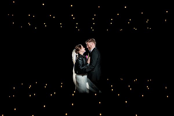 Couple embracing amidst twinkling lights in darkness.
