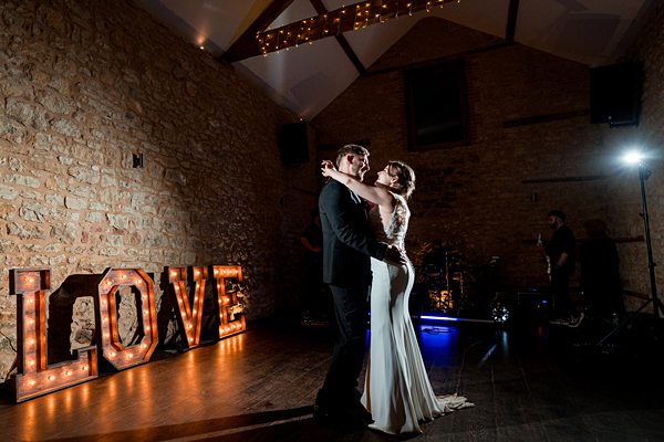 Couple dancing at wedding, love sign illuminated.