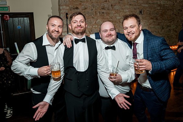 Four men smiling at event with drinks