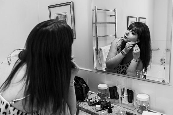 Woman applying makeup in bathroom mirror.