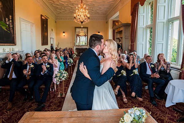 Couple's first kiss at wedding with guests applauding.