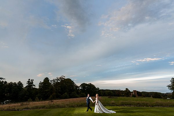 Couple walking in field on wedding day, scenic skies.