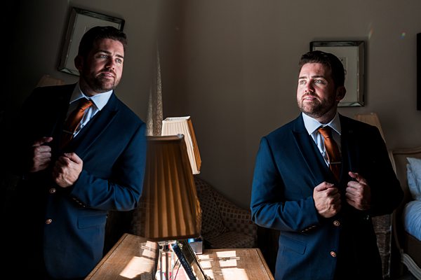 Man in suit adjusting tie near mirror.