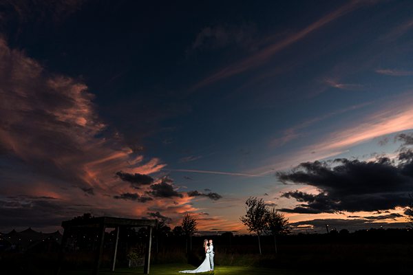 Couple under sunset sky at outdoor wedding ceremony.