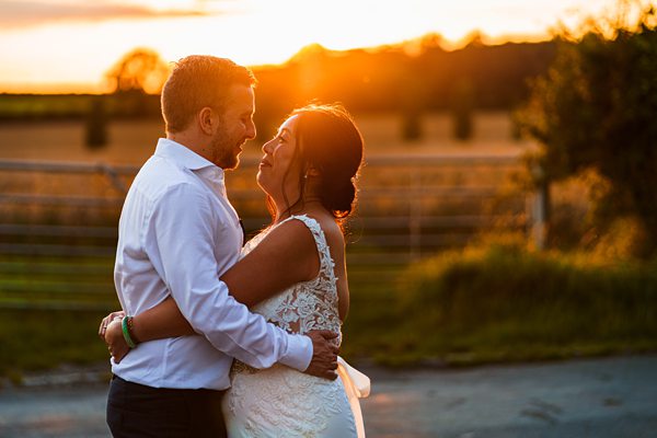 Couple embracing at sunset in countryside wedding.