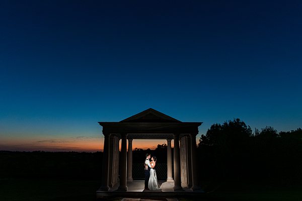Couple embracing at dusk in classical gazebo.