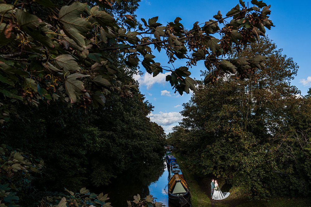 Canal boats and couple by the water under foliage.