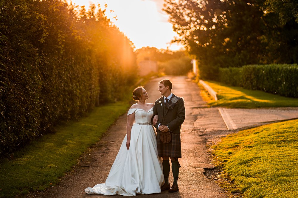 Couple in wedding attire enjoying sunset on garden path.