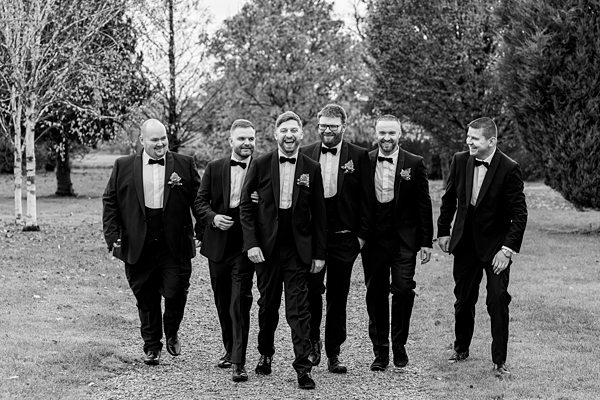 Group of men in tuxedos laughing outdoors.