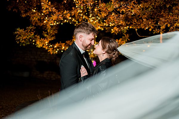Bride and groom kissing under illuminated tree at night.