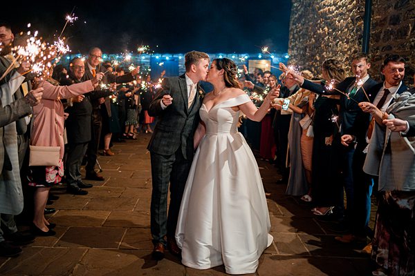 Bride and groom amidst sparkler send-off at evening wedding.