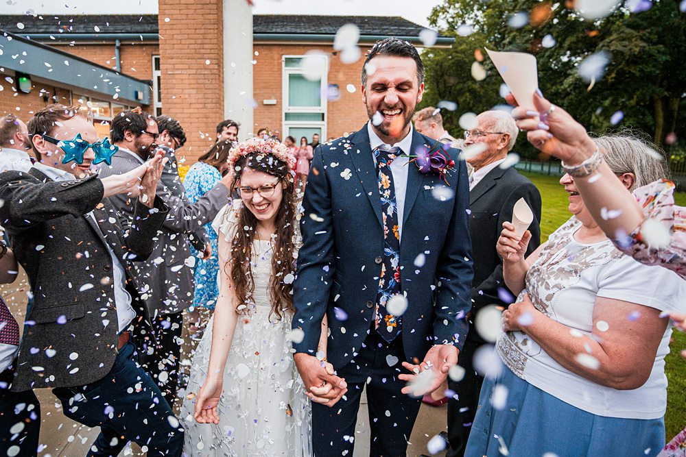 Joyful wedding couple with guests throwing confetti.