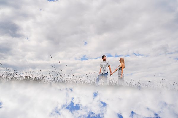 Couple holding hands in field under cloudy sky.