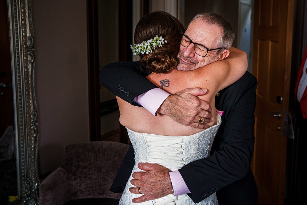 Emotional wedding hug with smiling elder man and bride.