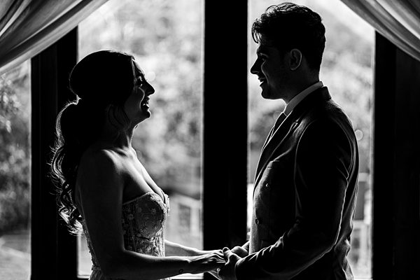 Couple silhouette in wedding attire holding hands.