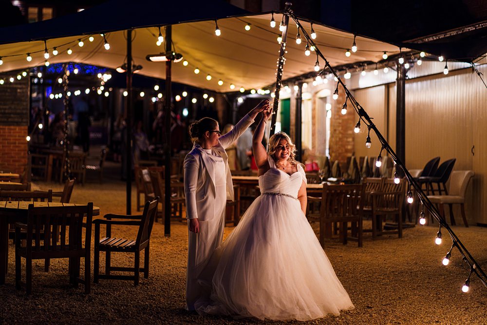 Brides dancing under string lights at evening wedding reception.