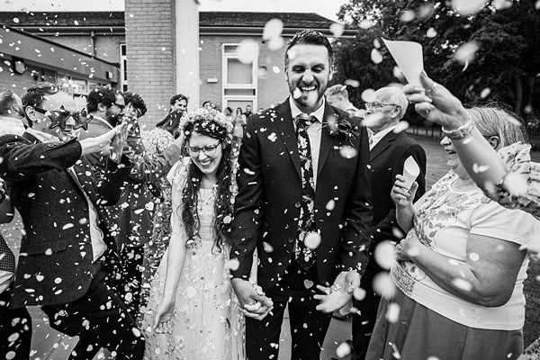 Couple smiling in wedding confetti shower.