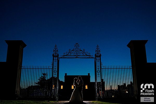 Silhouetted couple at gate of estate at dusk.