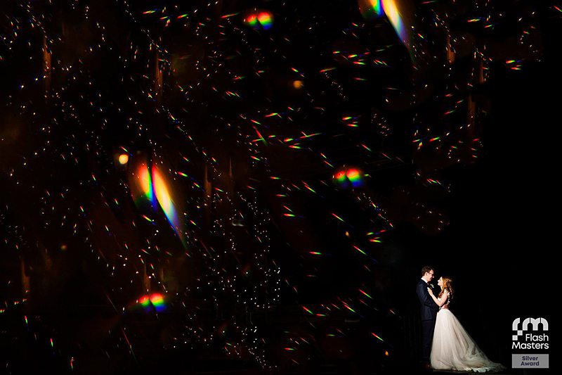 Couple embracing amidst sparkling lights at night.