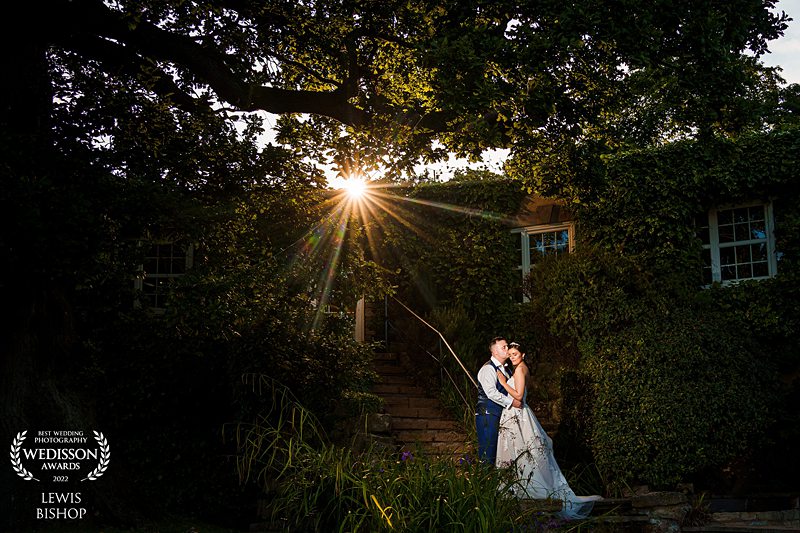 Couple kissing at sunset by ivy-covered house.