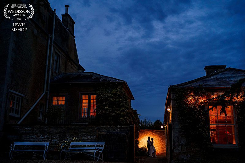 Evening wedding silhouette beside illuminated building.