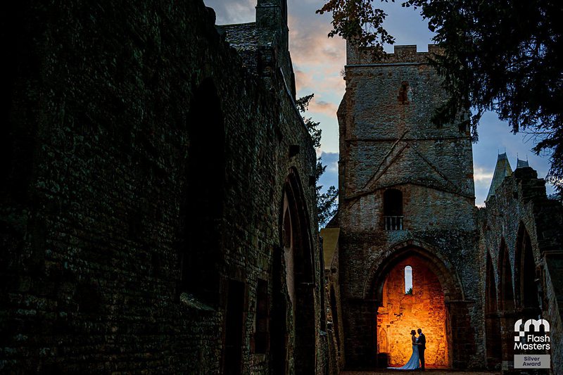 Couple embracing in illuminated archway of historic ruins at dusk.
