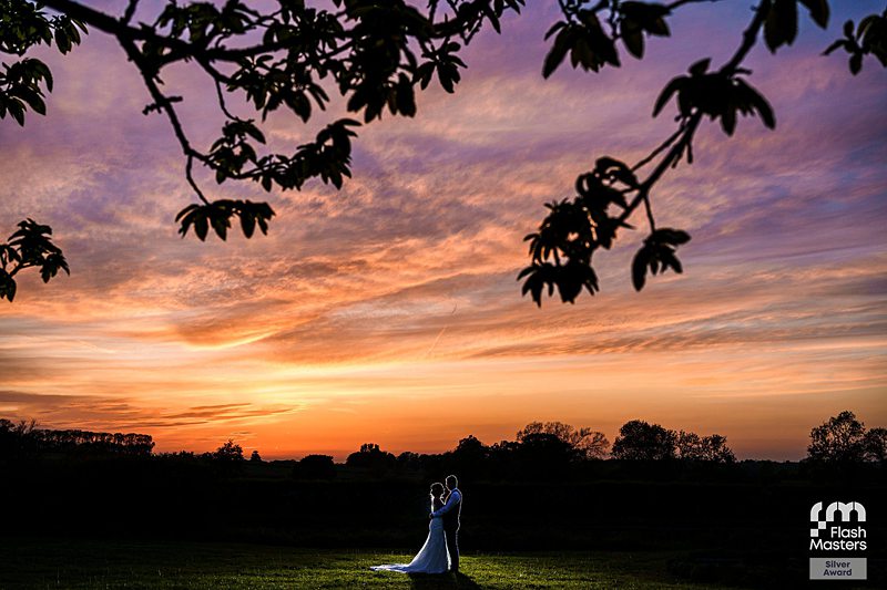 Couple embracing at sunset in countryside wedding scene.