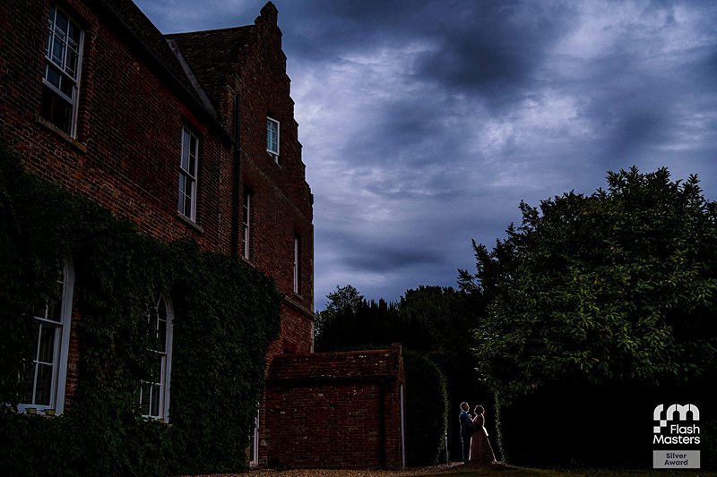 Couple embracing by historic brick manor at dusk.