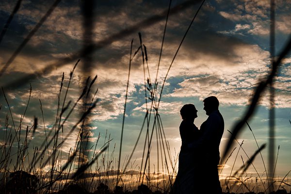 Silhouetted couple at sunset among tall grass.