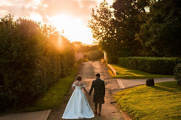 Couple in wedding attire walking at sunset.