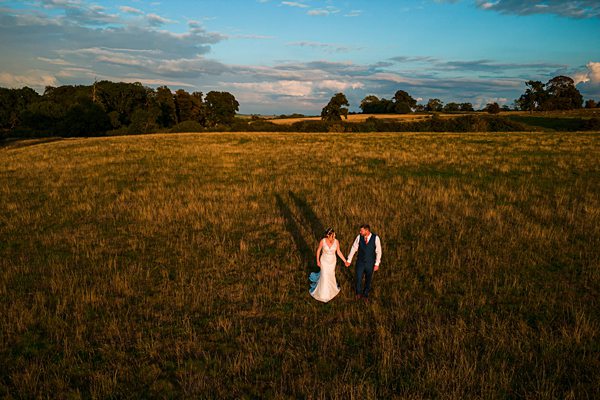 Couple holding hands in sunlit field at sunset.