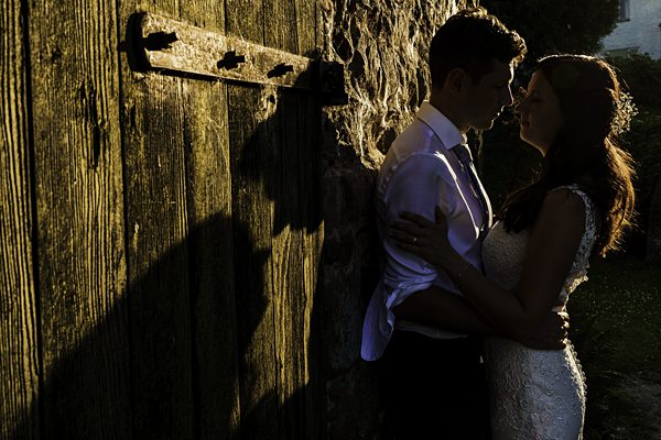 Couple embracing near rustic wooden door at sunset.