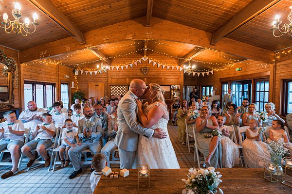 Bride and groom kissing at rustic wedding ceremony.