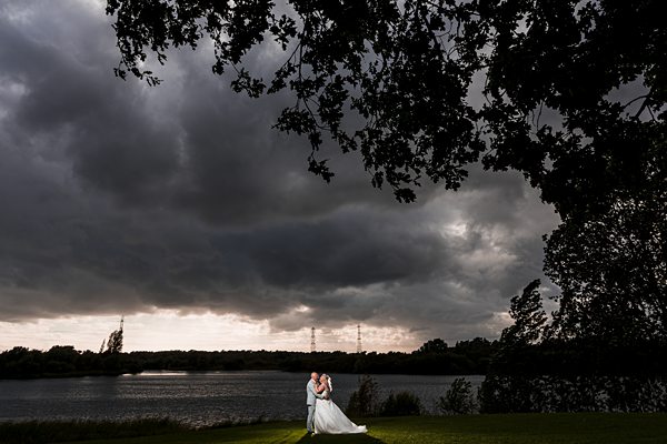Couple embracing by lake under dramatic stormy sky