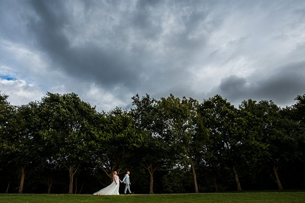 Wedding couple walking under dramatic sky in park.