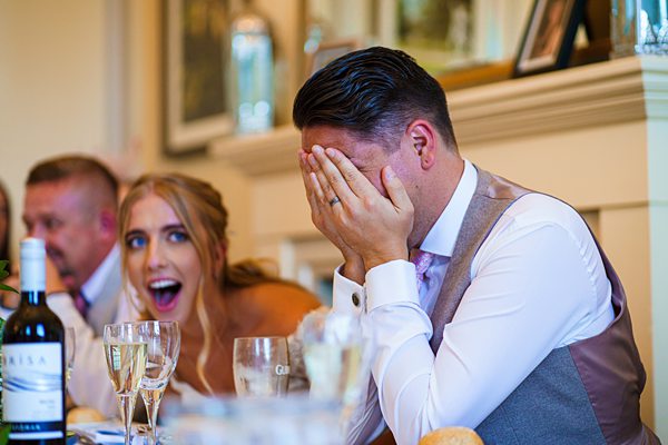 Man covering face, woman laughing at wedding table.