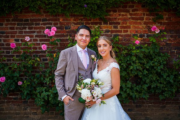 Couple posing at wedding with brick wall and roses.