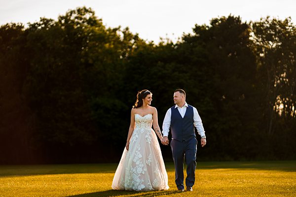 Bride and groom walking in sunset light on field