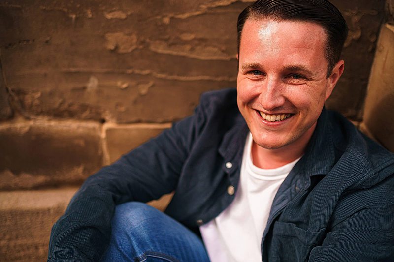 Man smiling sitting by brick wall.