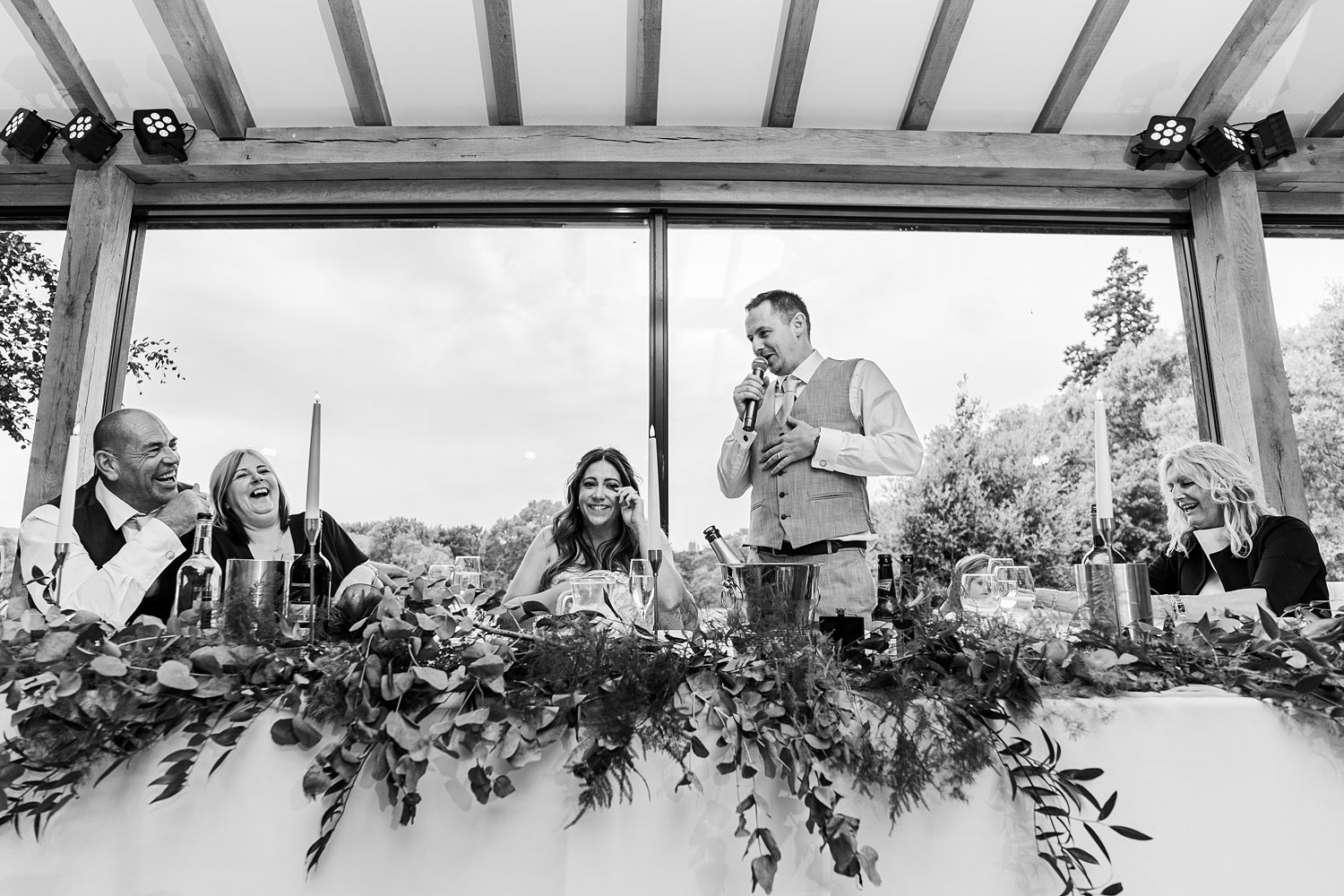 Joyful wedding speech, guests laughing, outdoor reception.