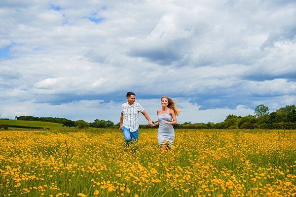 Couple running through wildflower meadow under blue sky.